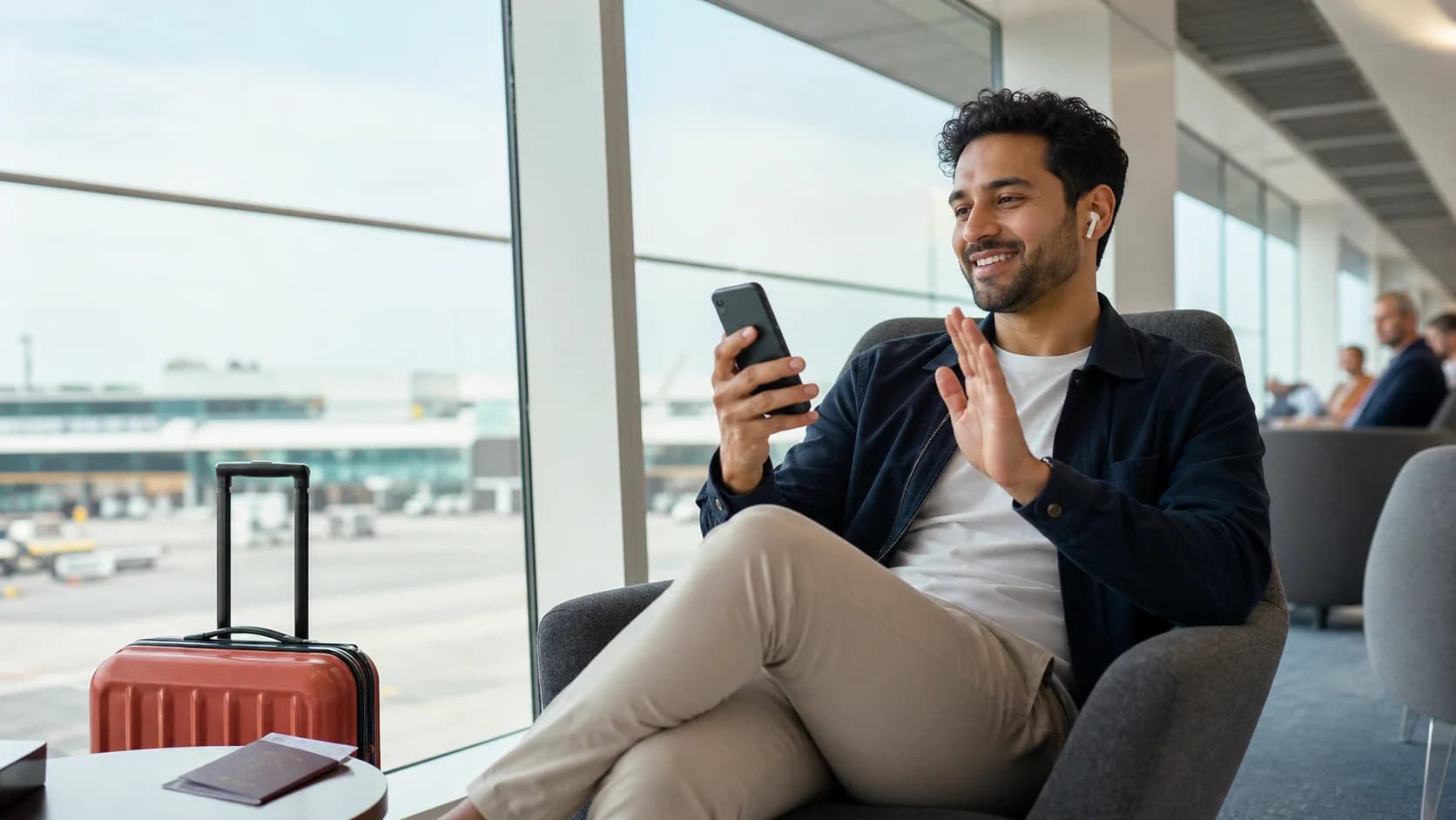 Traveler making a video call on a phone in a bright airport lounge beside carry-on luggage